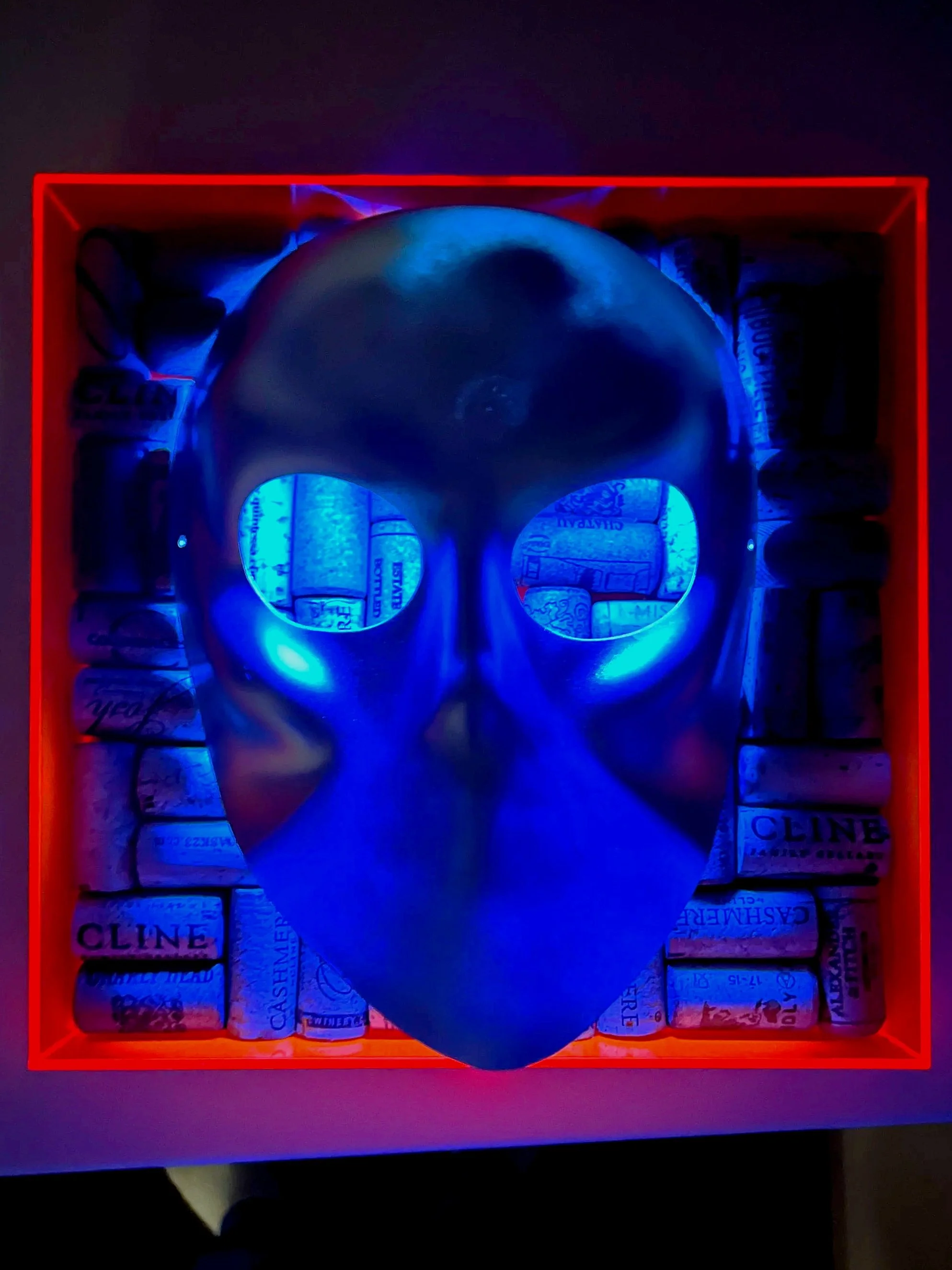 A metallic skull mask with glowing blue eyes, placed inside a red box filled with cigarrete packs.