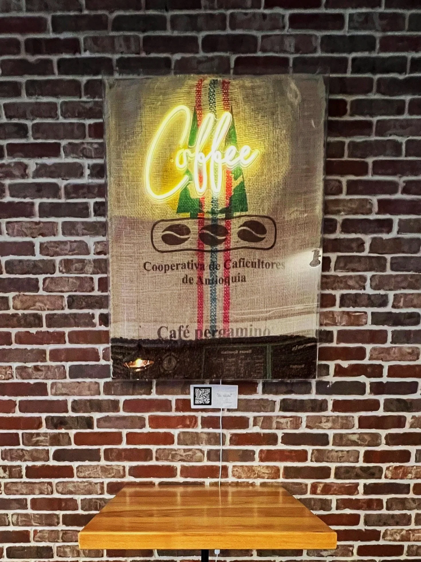 Neon sign that reads 'Coffee' with a stylized coffee tree and coffee beans, mounted on a brick wall above a small wooden table.