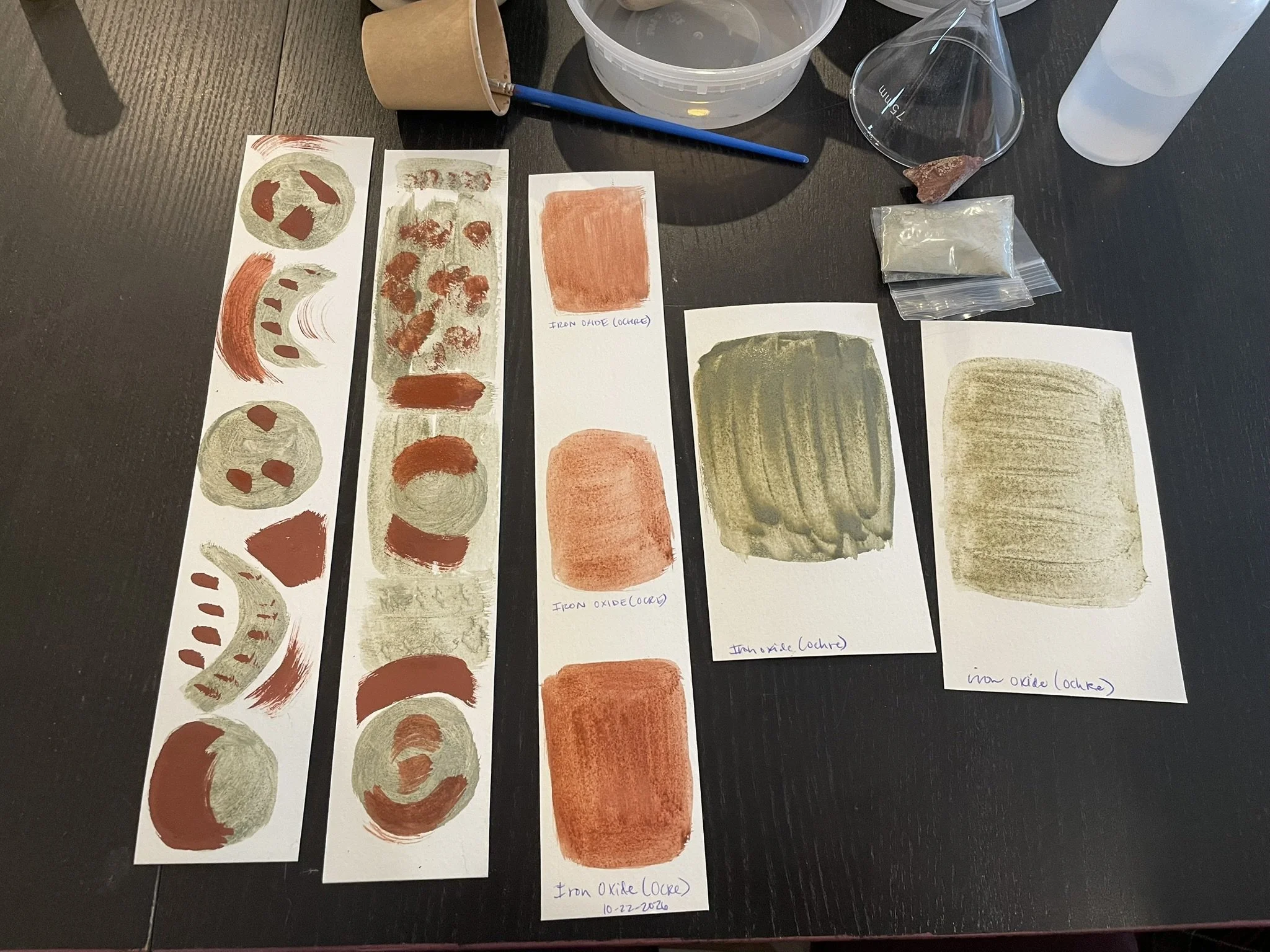 Painted swatches of earth pigments in shades of red, orange, yellow, and gray