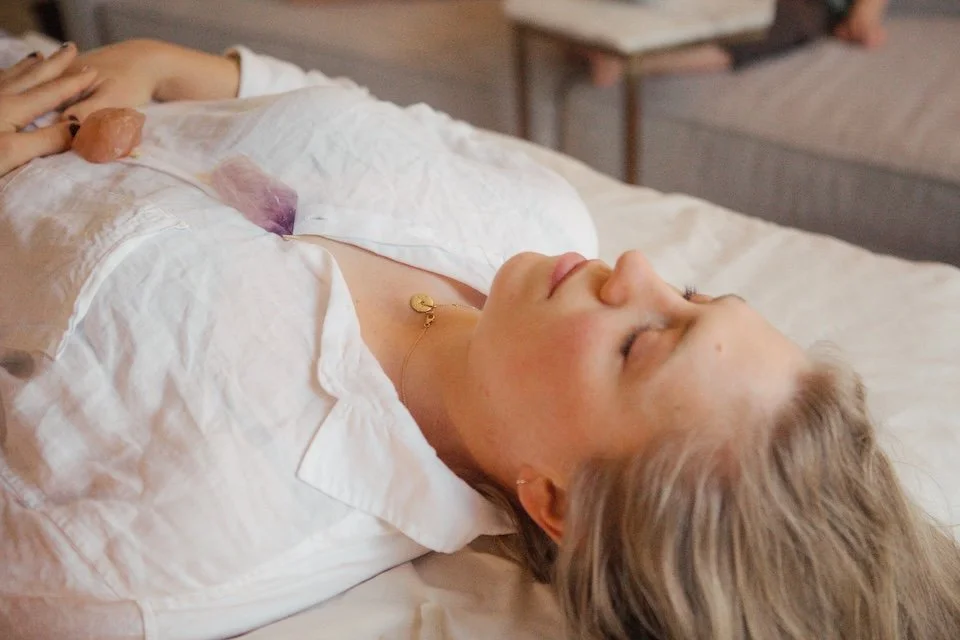 A woman lying on a bed with her eyes closed, wearing a white shirt and a necklace.