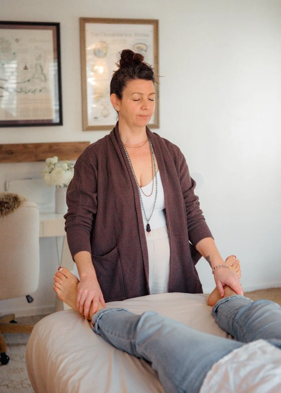 Erin providing CranioSacral Therapy services to someone lying on a massage table in a cozy, well-lit room decorated with framed artwork and a flower arrangement.