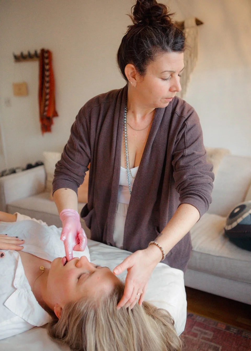 A woman providing a medical or dental procedure to a patient lying on a bed in a cozy room.