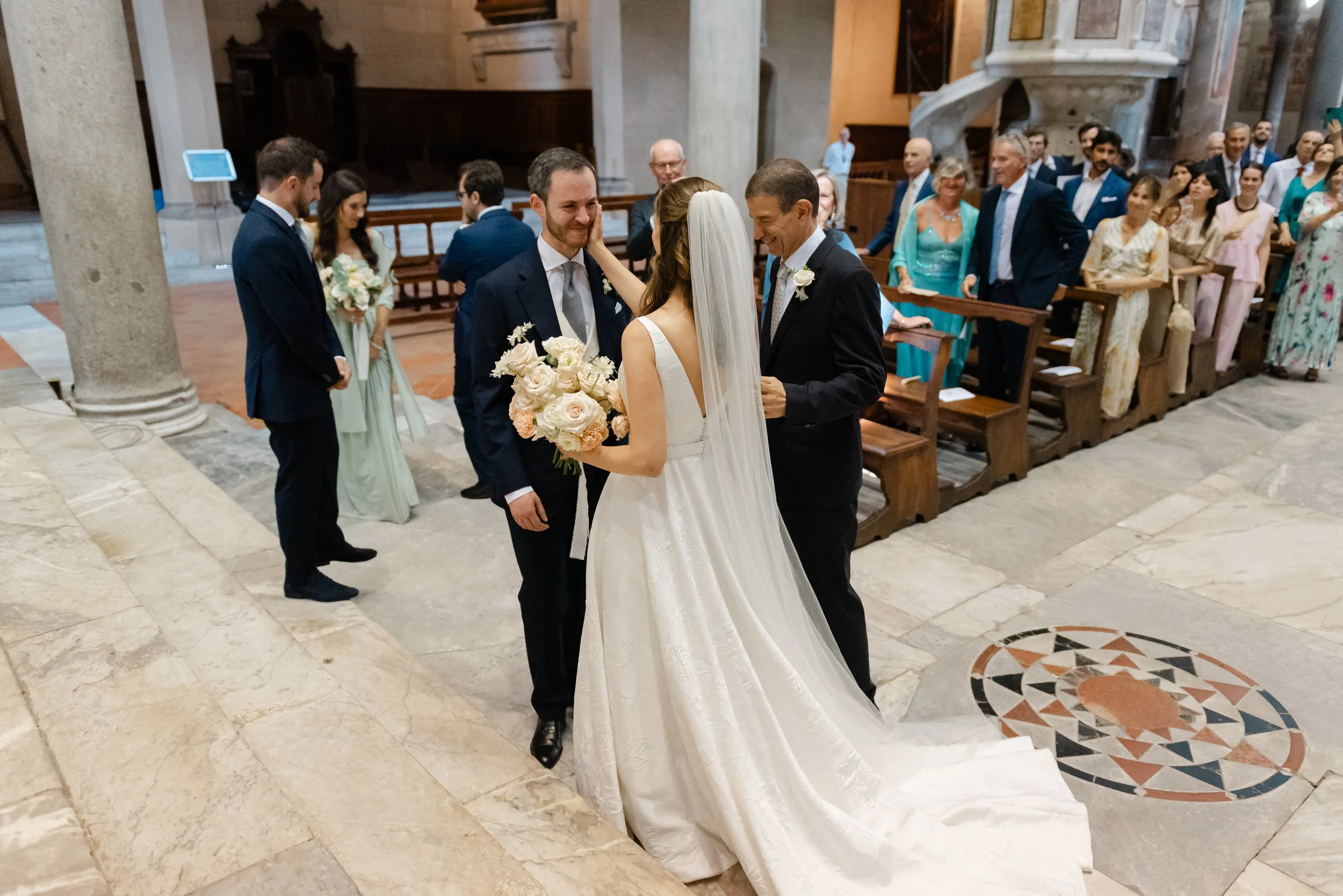 Una coppia di sposi in chiesa durante il matrimonio, con il sacerdote che annuncia la cerimonia mentre gli invitati osservano.
