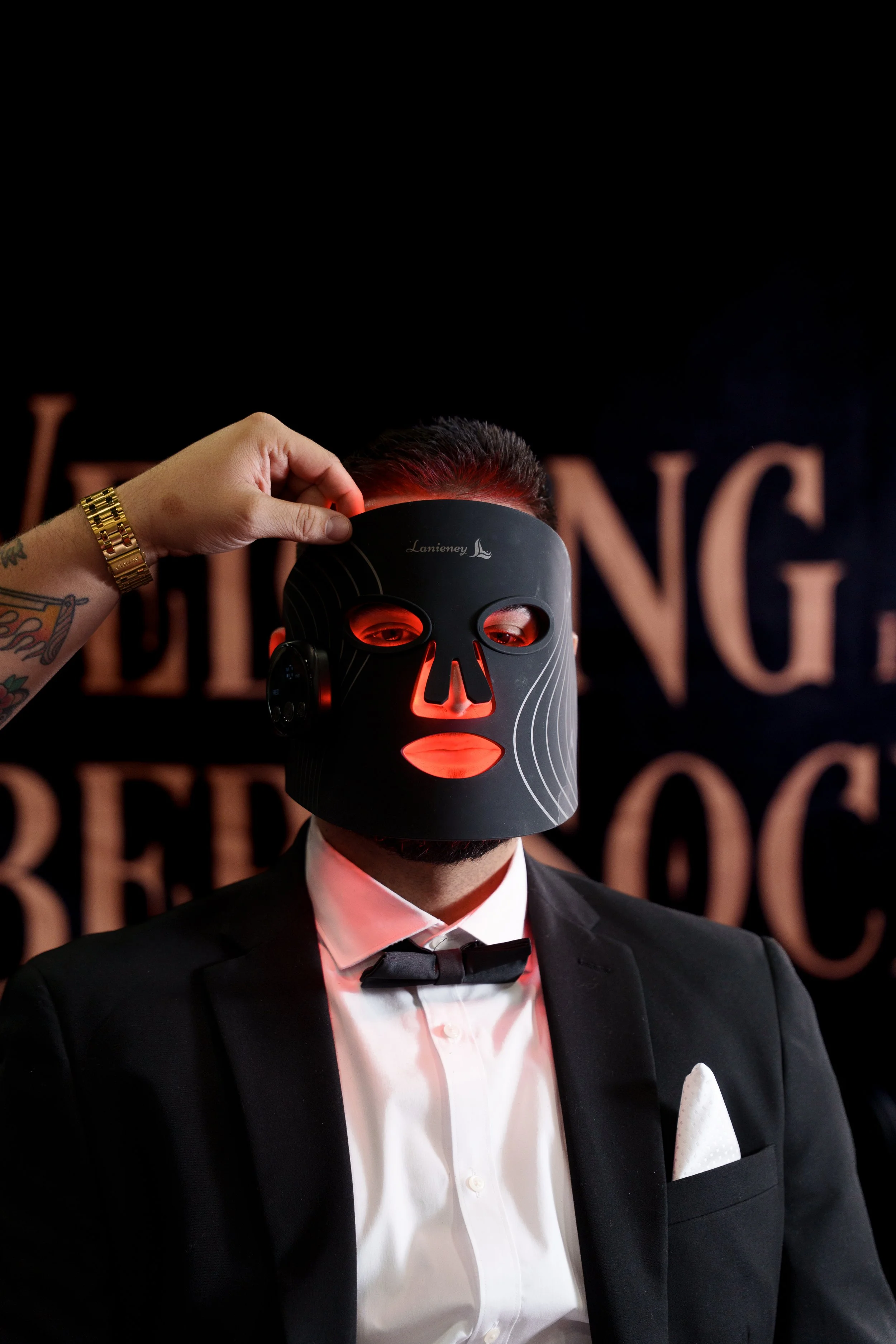 A man with curly hair and a beard lying back with his eyes closed while a person applies sunscreen to his face in a barbershop or salon.