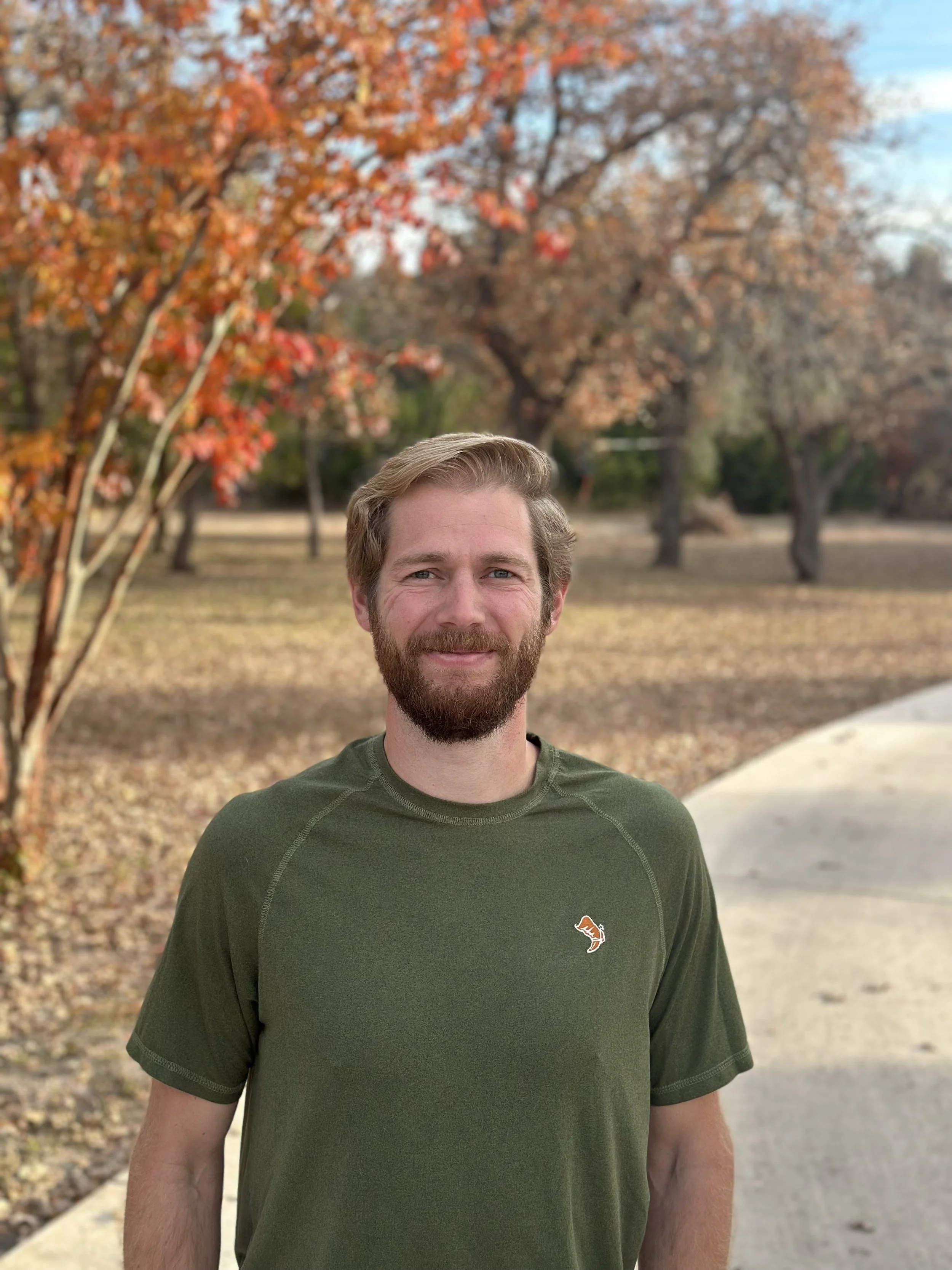 A headshot of Jeff Graham with a beard and light brown hair standing on a sidewalk with autumn trees in the background.
