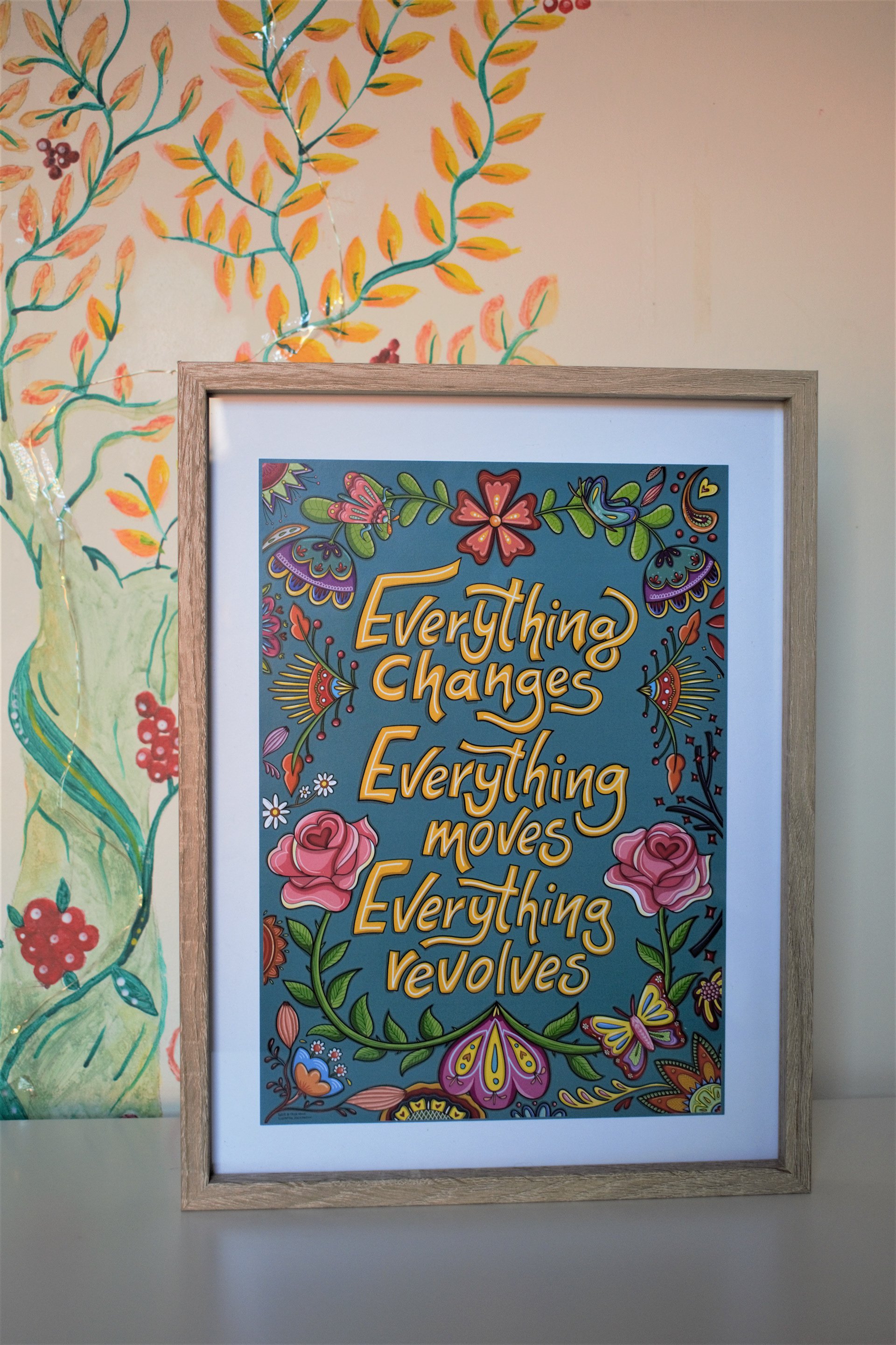 Colorful framed poster with floral and butterfly illustrations containing the quote 'Everything changes, everything moves, everything revolves'.