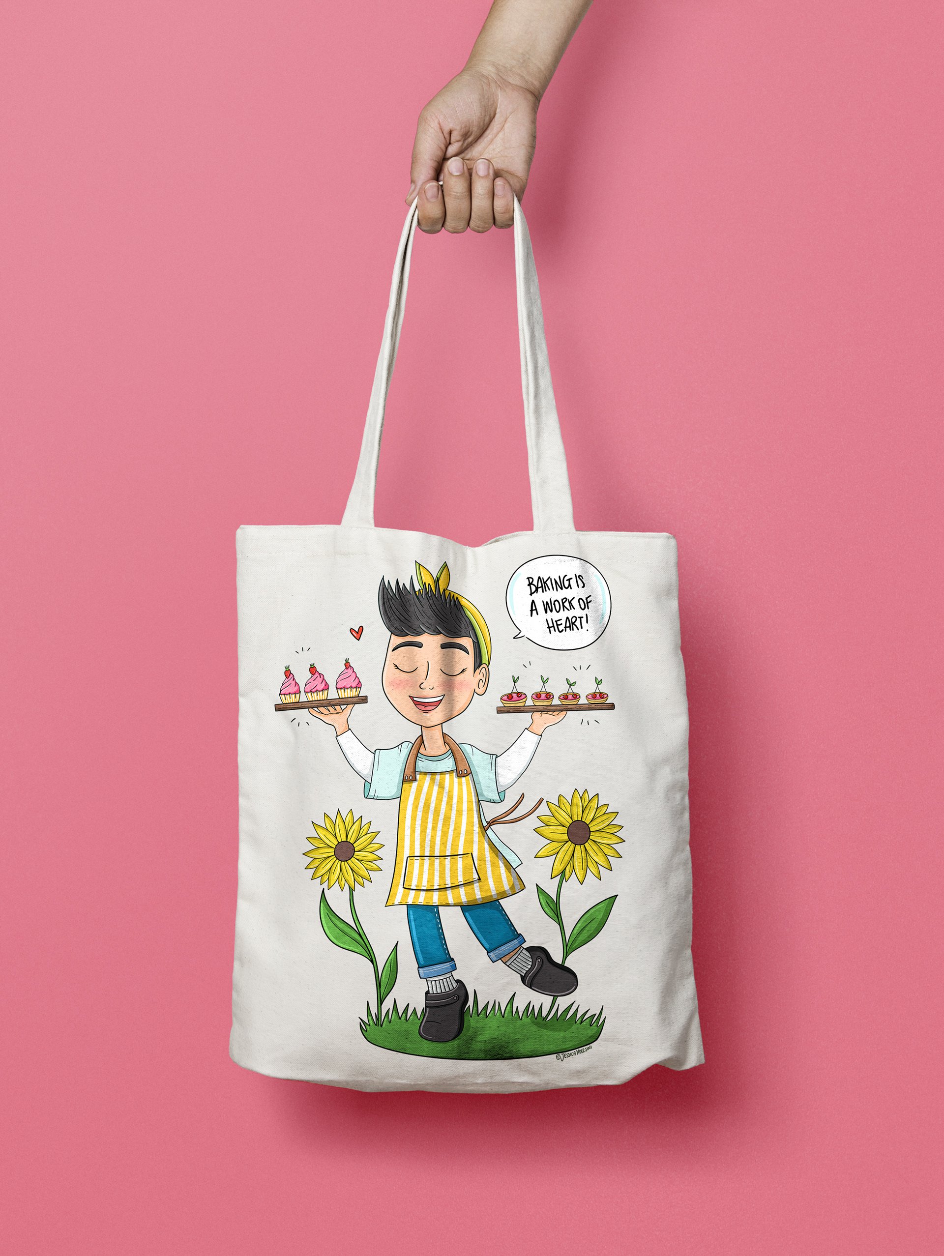 A tote bag featuring a cartoon illustration of a person holding two trays of cupcakes and small plants. The person is smiling, wearing a yellow striped apron, and standing on grass with sunflower flowers around them. The illustration includes a speec