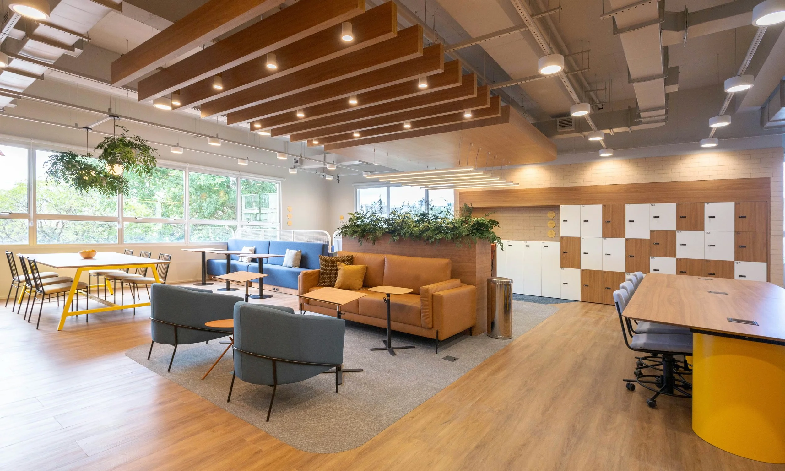 Espaço de coworking com sofás, mesas de trabalho, armários de armazenamento e iluminação moderna.