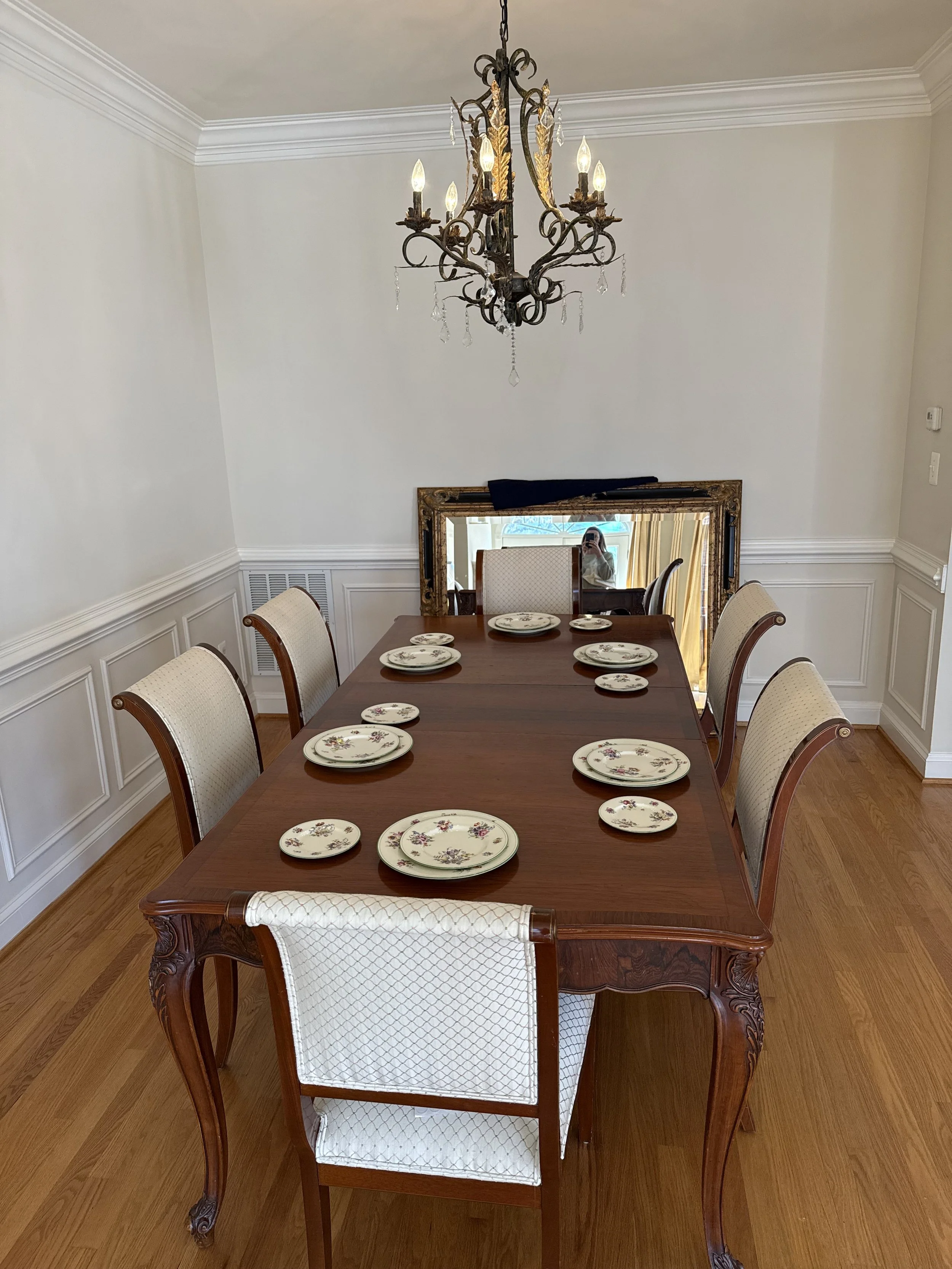 A classic dining room setup in a rental home featuring a wooden dining table, white upholstered chairs, and an ornate vintage chandelier.