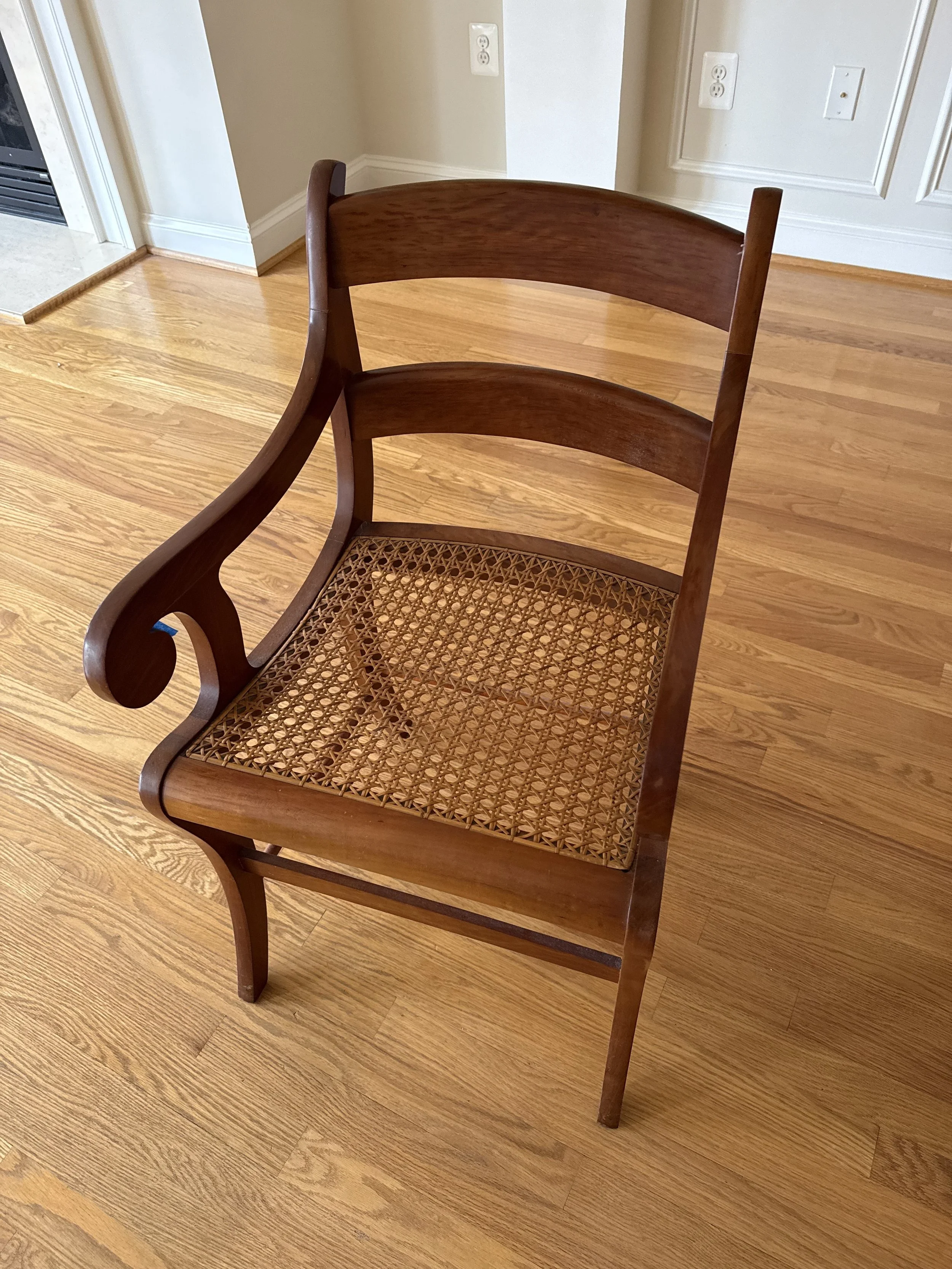 A thrifted vintage wooden armchair with a woven cane seat sitting on hardwood floors, sourced for a curated, timeless interior.