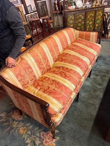 A vintage sofa with red and gold striped upholstery and a wooden frame, discovered while thrifting for high-quality forever pieces.