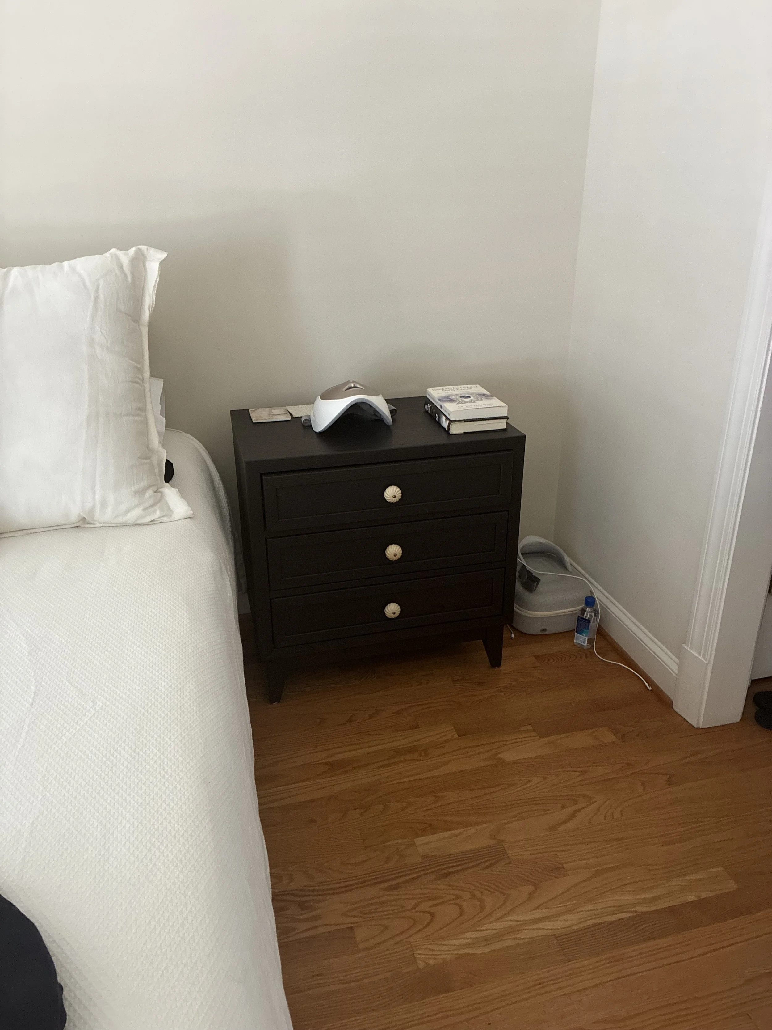 A dark painted bedside table with gold hardware next to white bed linens, highlighting a budget-friendly DIY furniture upgrade for a rental bedroom.