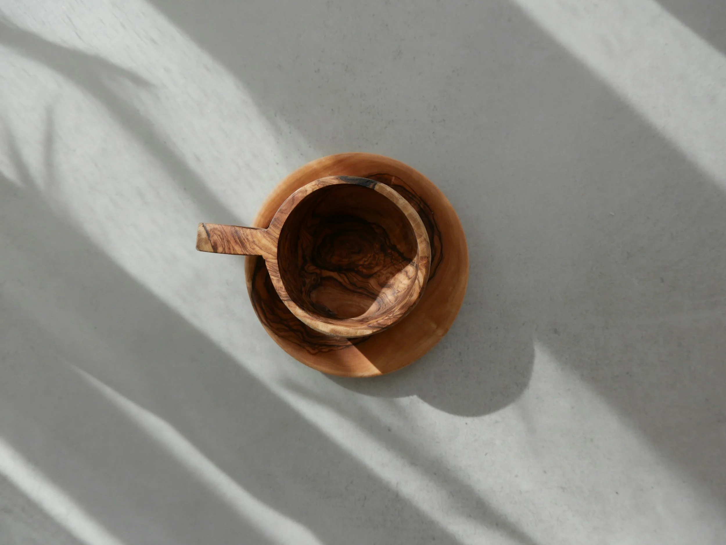 Top-down view of a wooden cup and saucer on a light gray surface with shadows.