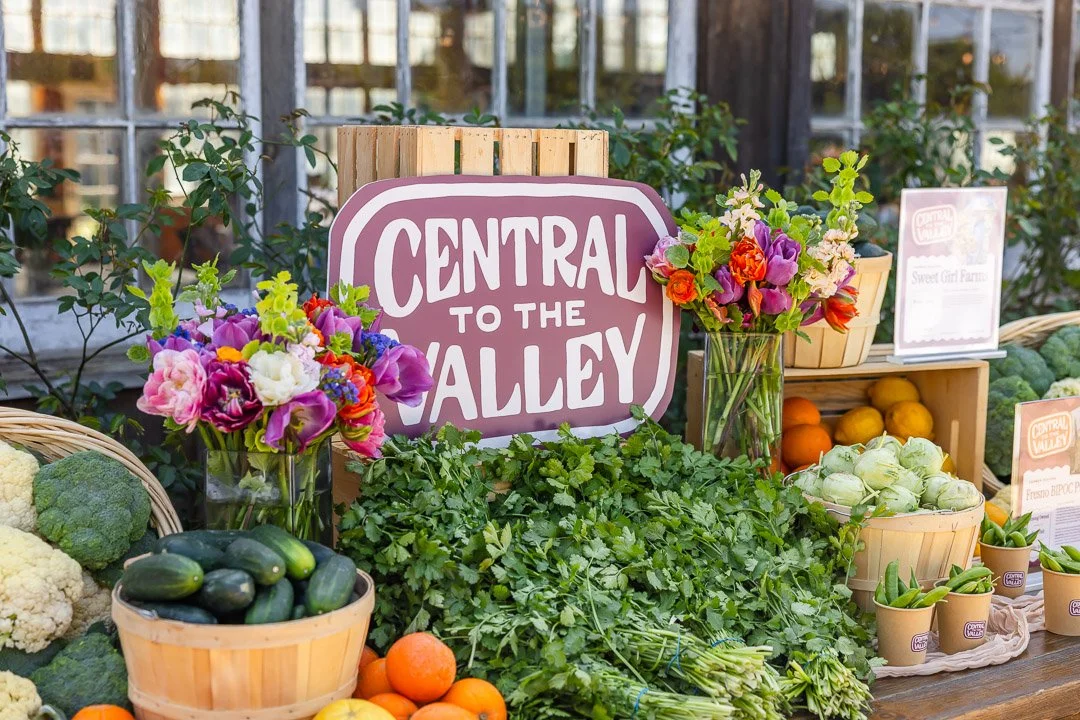 Fresh vegetables and flowers on display at a farm stand with a sign that reads "Central to the Valley."