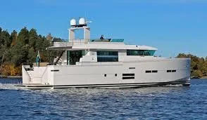 Modern white yacht on water with a blue sky and trees in the background.