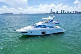 A white yacht anchored in clear green water with a city skyline in the background.