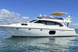 A large white yacht with a beige sunshade on the deck, floating on calm water under a partly cloudy blue sky.