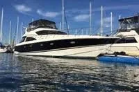 Large white yacht docked at a marina with sailboats nearby, under a blue sky.