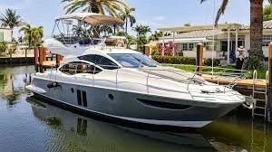 Luxury yacht docked in a canal with palm trees and modern houses in the background.