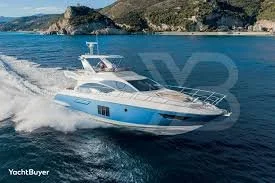 A white and blue motor yacht cruising through the ocean with land and cliffs in the background.