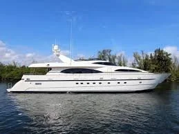 Large white yacht docked on the water with trees and blue sky in the background
