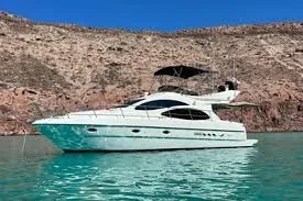 Luxury white yacht anchored near a desert coastline with rocky hills in the background.