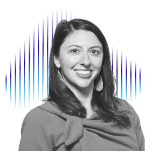 Black and white portrait of a woman smiling, with long dark hair, wearing earrings and a top with a bow, in front of a blue digital background.