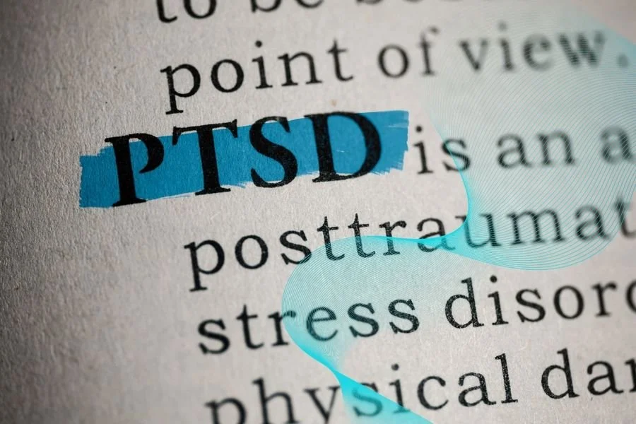 Close-up of a printed page with the word 'PTSD' highlighted in blue, surrounded by partially visible text about trauma and stress.