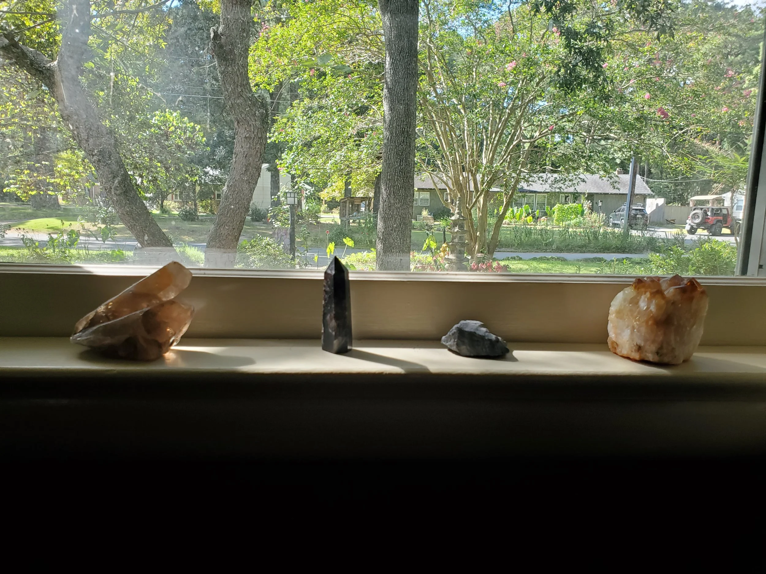 Collection of five mineral or crystal specimens on a windowsill with trees and houses outside.
