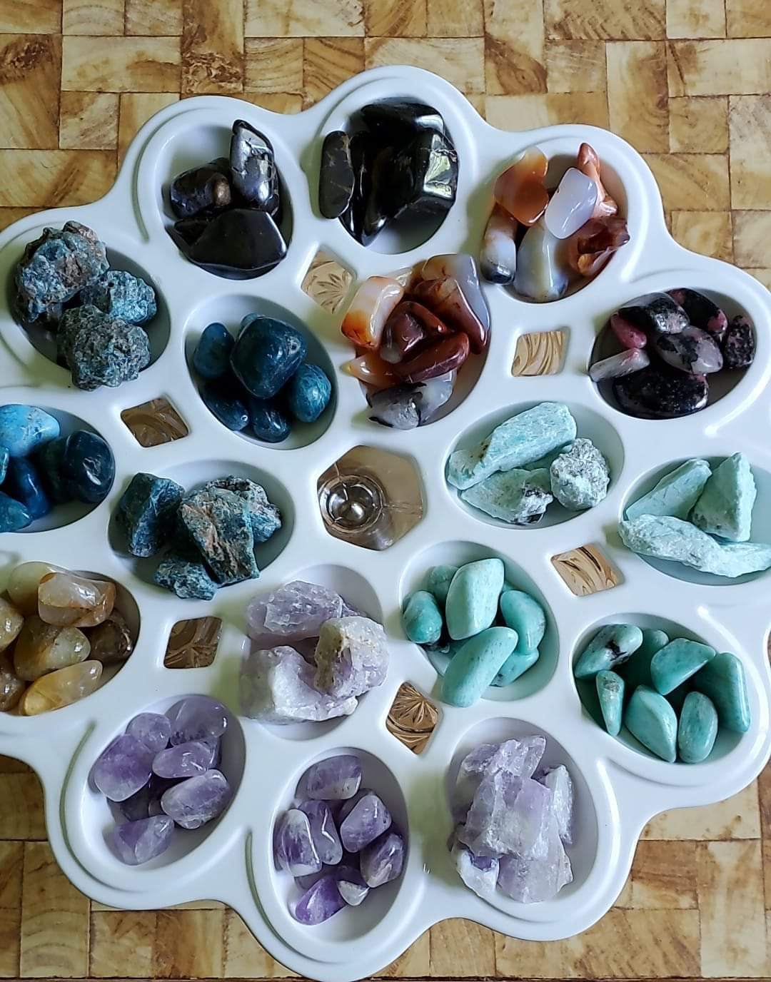 A white gemstone display tray with various types of polished stones in separate compartments on a wooden surface.
