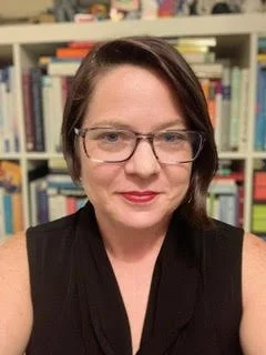 Person wearing glasses in front of a bookshelf.