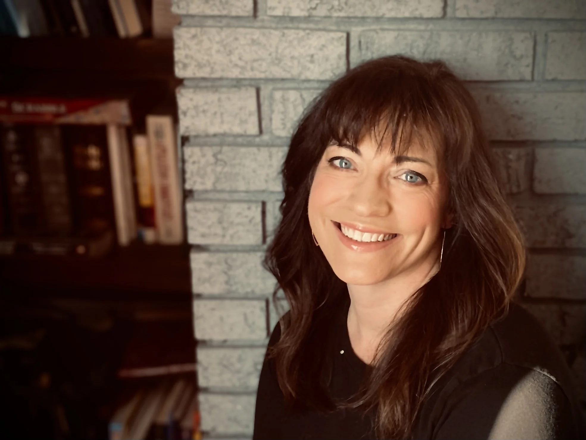 Smiling woman with dark hair in front of a brick wall and bookshelf