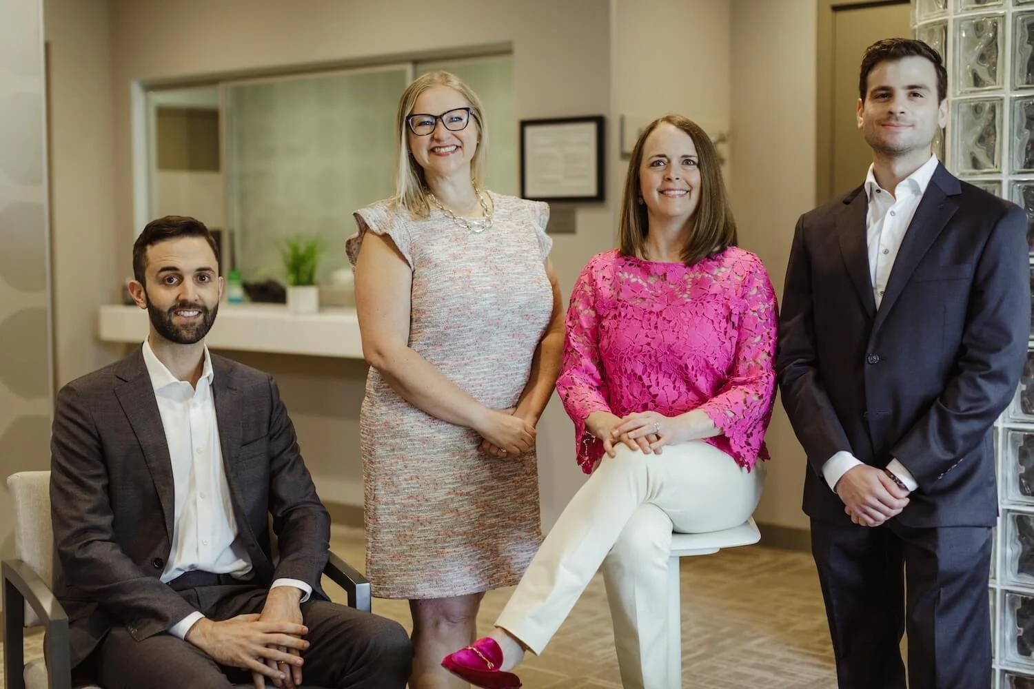 Group of four professionally dressed people posing indoors, two men and two women, smiling at the camera.