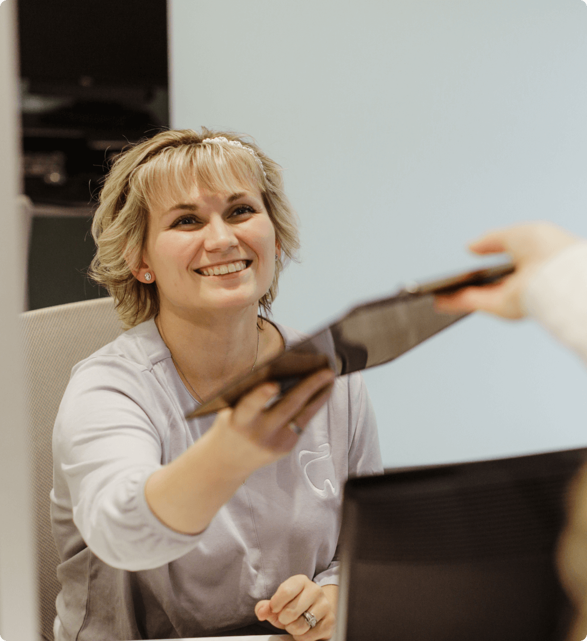 Friendly receptionist at the Center for Oral Surgery + Dental Implants hands forms to patient on a clipboard