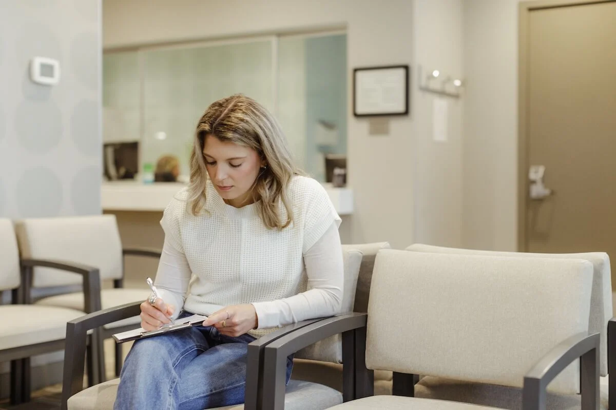 Woman sitting in a waiting room, writing on a notepad.
