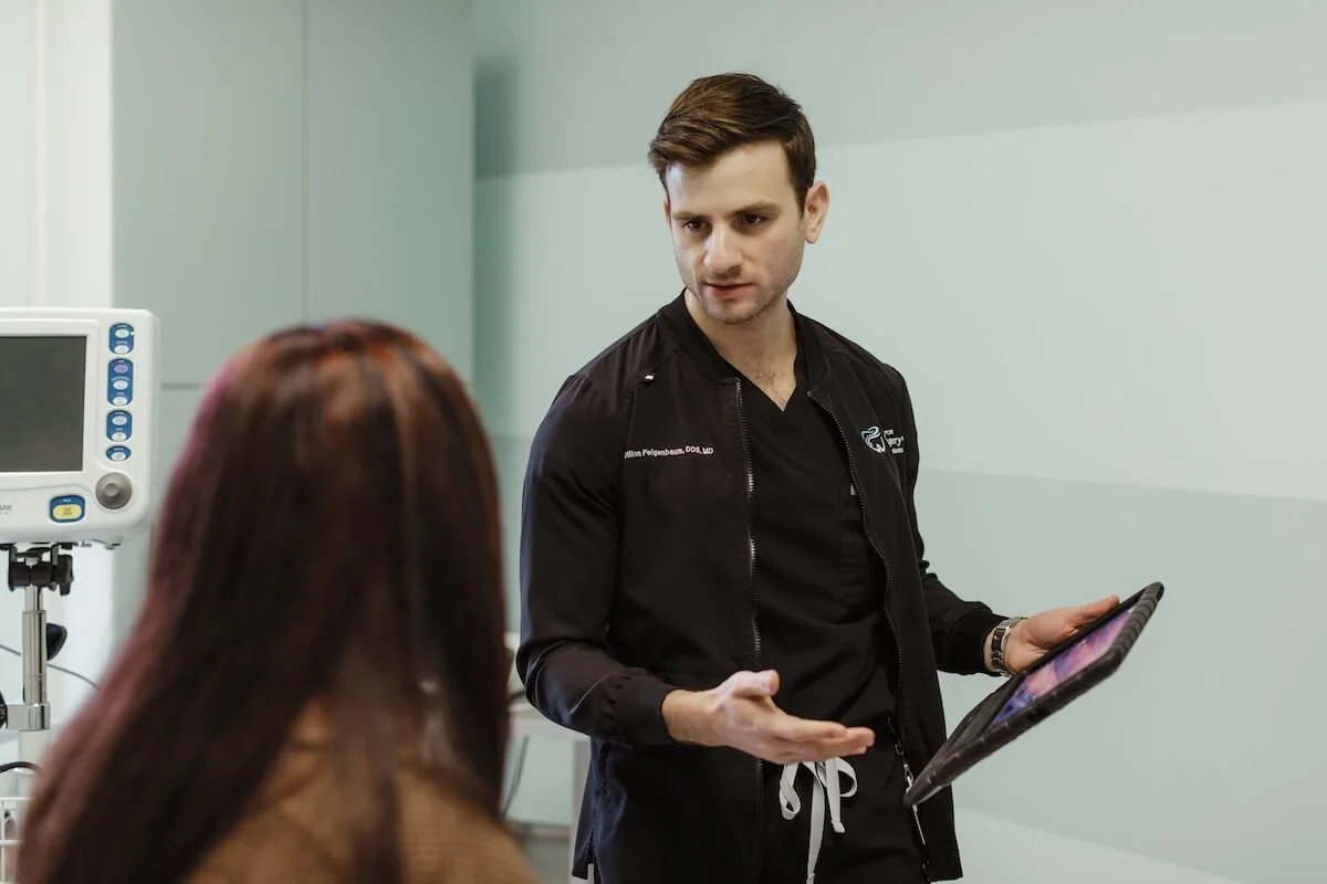 A male doctor holding a digital tablet talking to a female patient in a medical office.