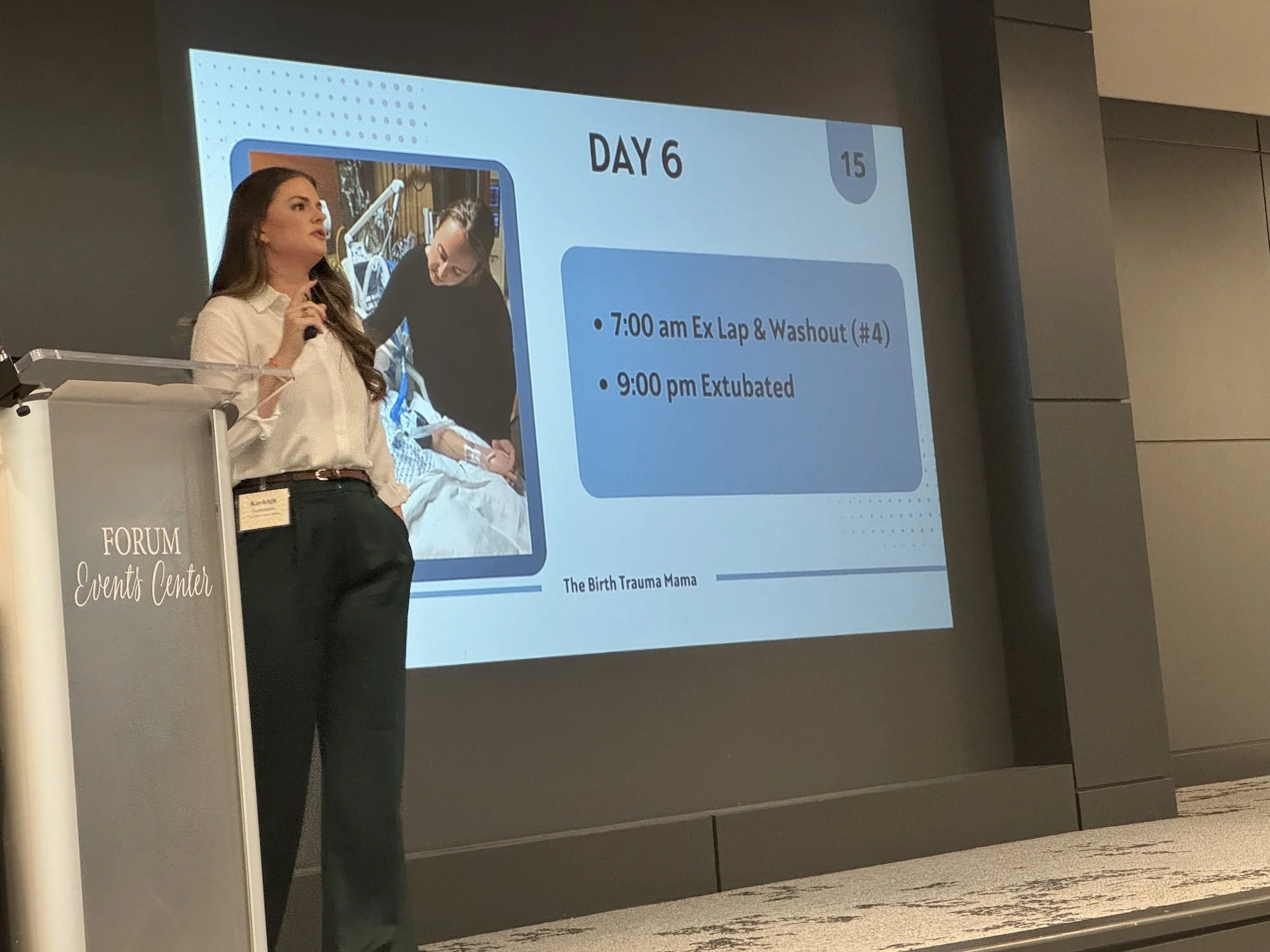 A woman giving a presentation about Day 6 of a program, with a slide showing schedule times and activities, including '7:00 am Exit Lap & Washout' and '9:00 pm Extubated,' at a conference or seminar in a forum events center.