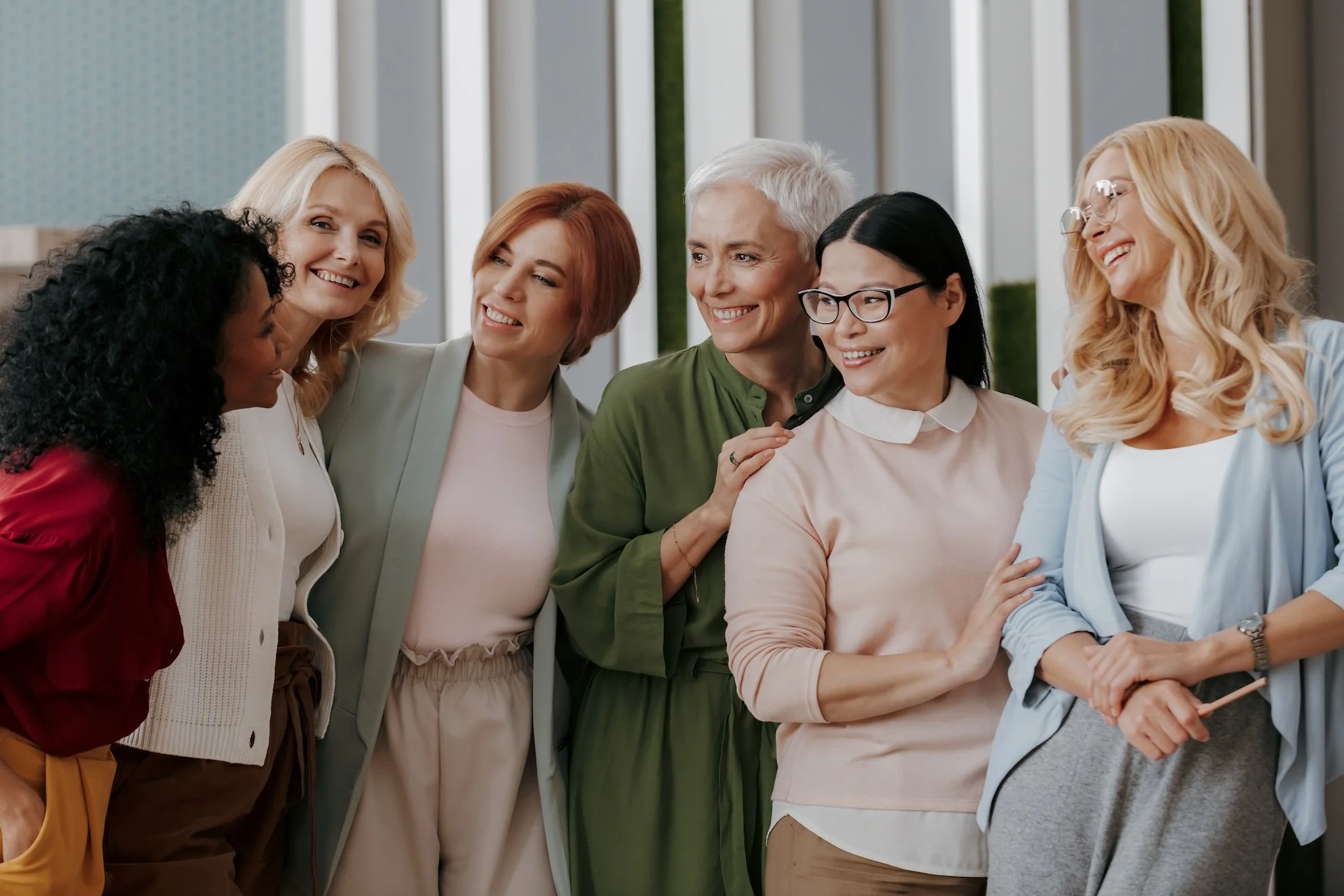 Group of diverse women gathered together, smiling and talking in a bright modern indoor space.