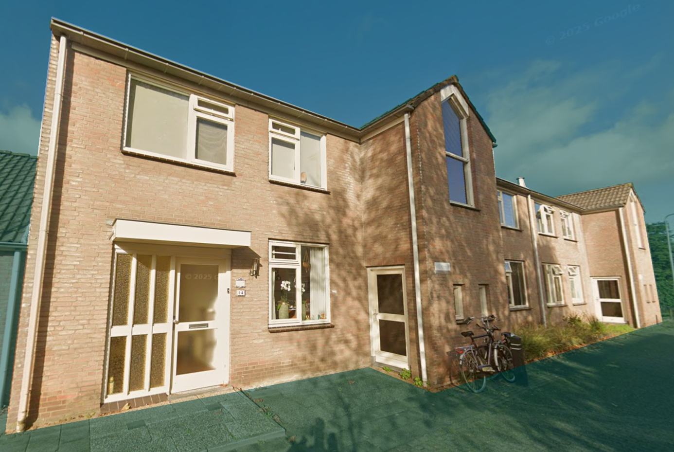 A row of brick townhouses with white doors and windows, bicycles parked outside, and a green lawn, under a partly cloudy sky.