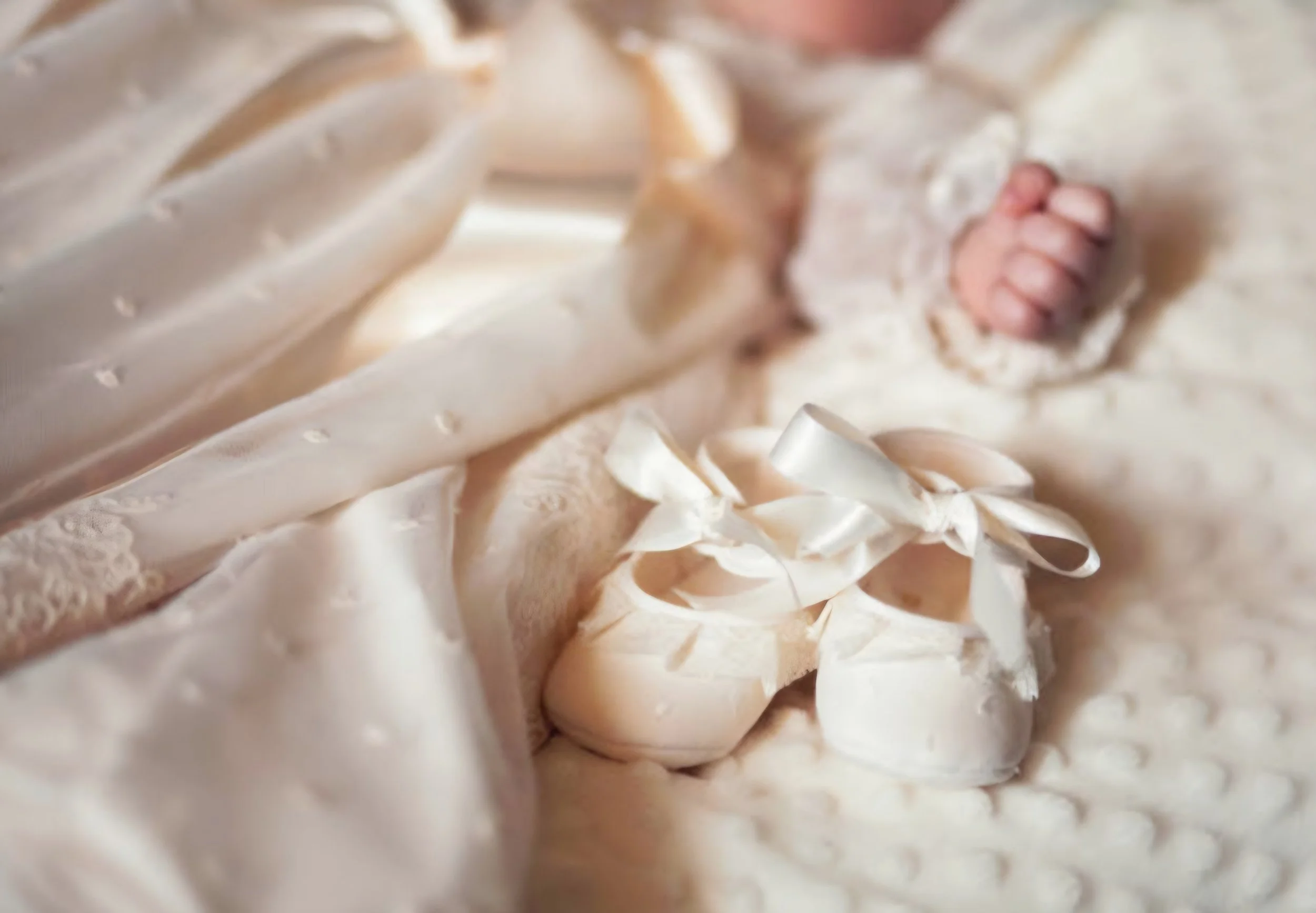 Close-up of a baby dressed in a creamy, textured outfit with lace and bow details, lying on a soft surface.