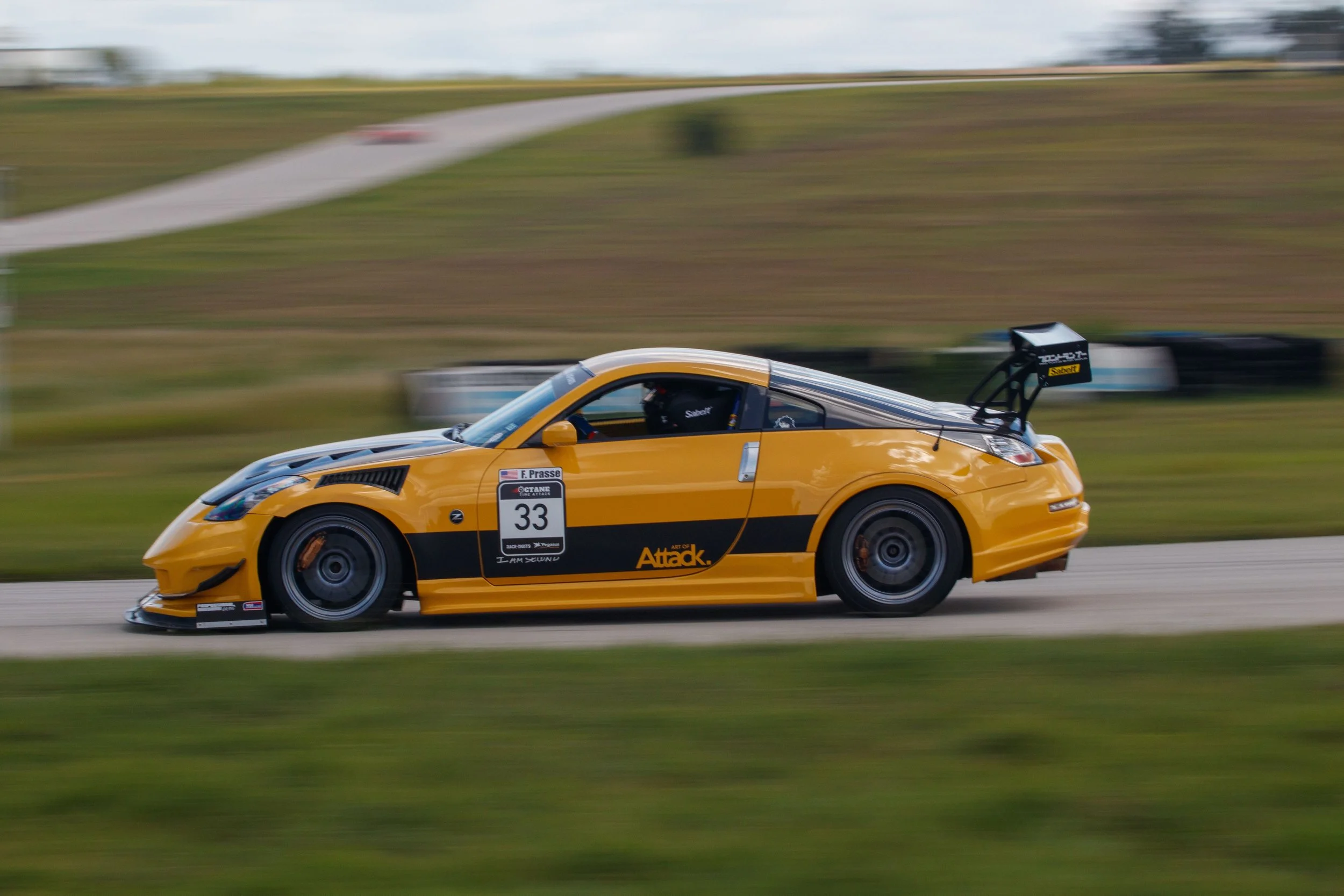 A yellow race car with black accents driving on a racetrack with a blurred background.