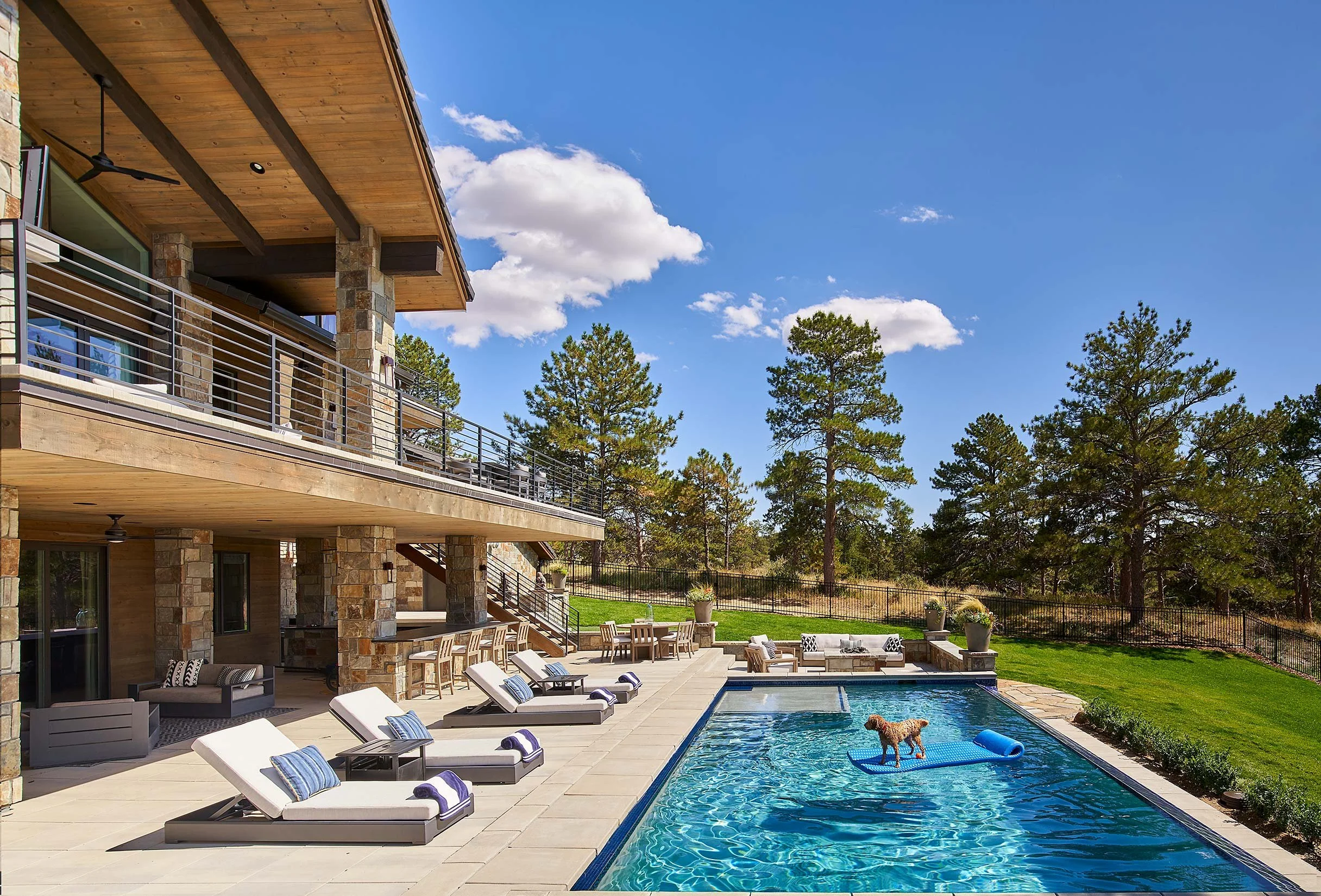Beautiful landscaping by Waymark showing a dog on a raft in a pool outside a two-story home.