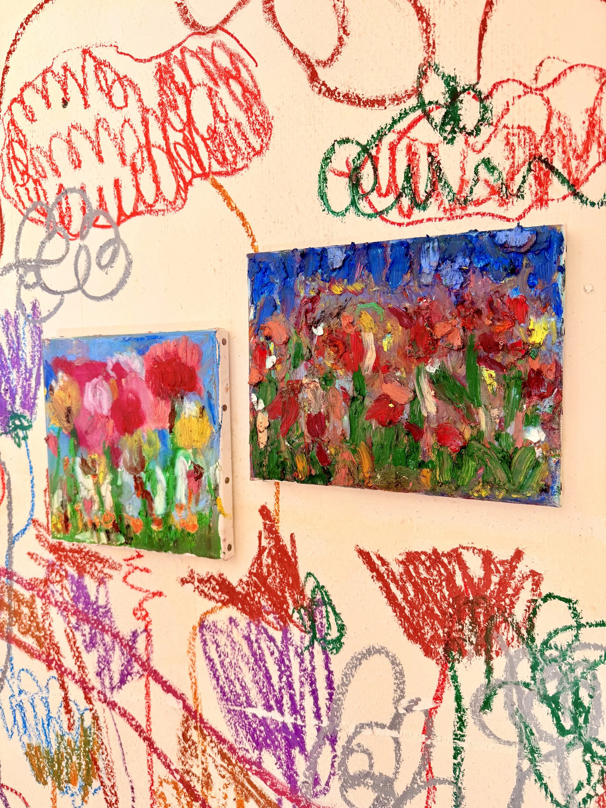 Colorful abstract paintings on a beige wall surrounded by crayon drawings of hearts, smiley faces, and other shapes.