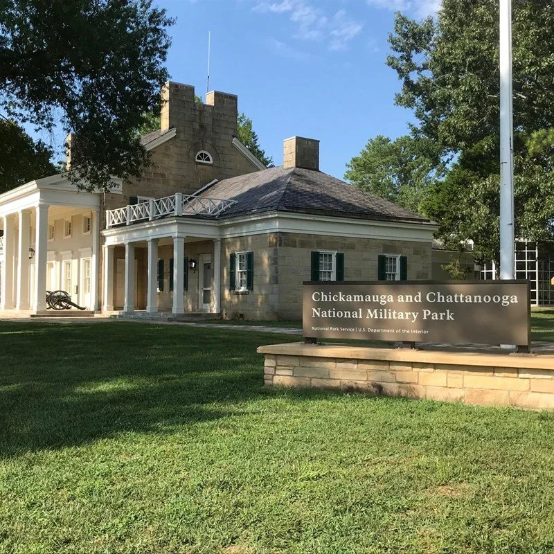 A historic stone building with a wraparound porch, black shutters, and a banner sign in front that reads, "Chickamauga and Chattanooga National Military Park."