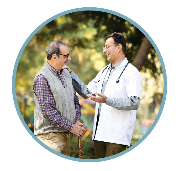 A doctor talking to an elderly man outdoors, smiling, with trees in the background.