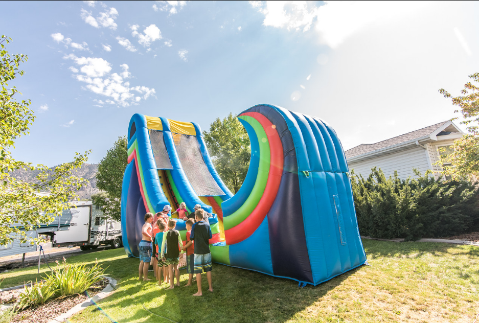 Children waiting in line to go down an inflatable water slide outdoors on a sunny day.