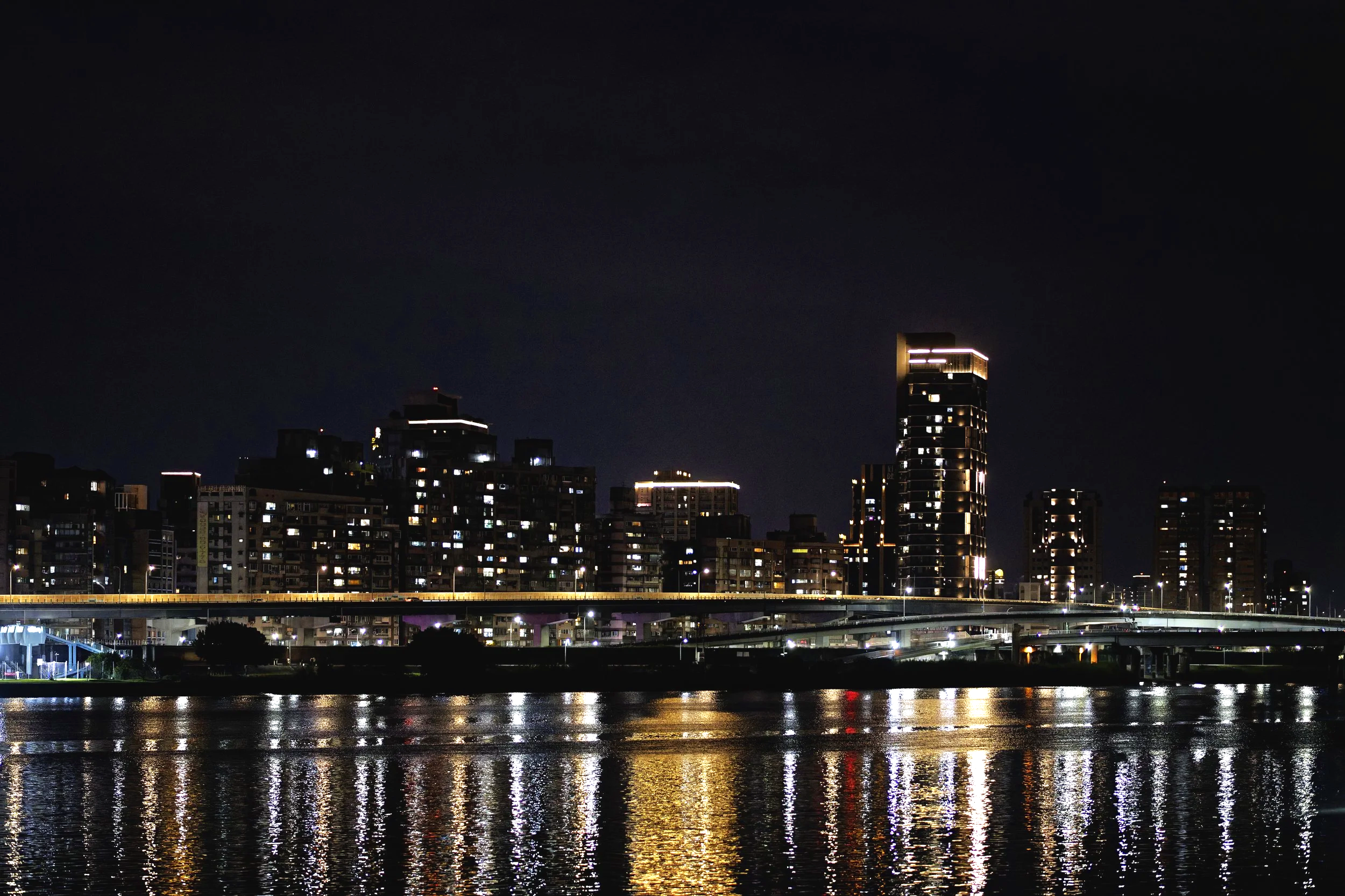 Nighttime cityscape with illuminated high-rise buildings reflecting on the water.