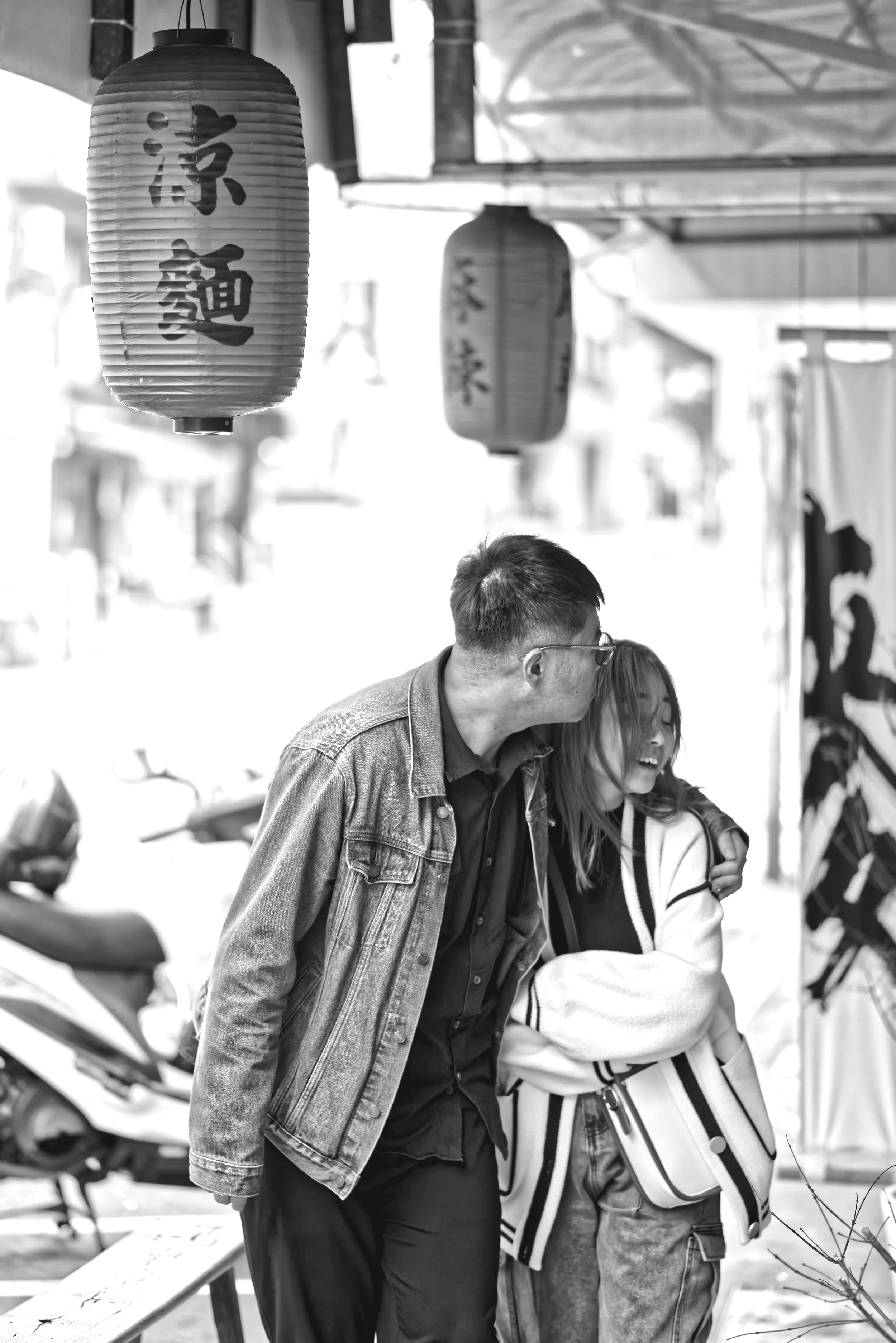 A man and woman laughing and hugging on a street with hanging lanterns, black and white photo.