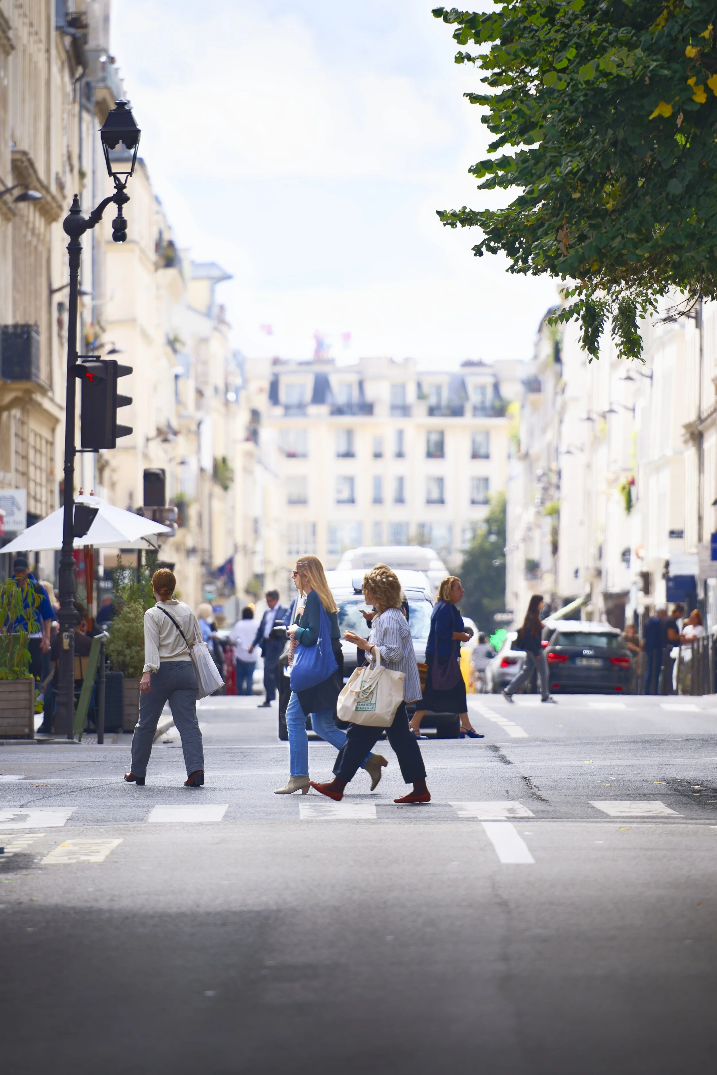 People crossing the street in a city, with tall buildings and cars in the background.