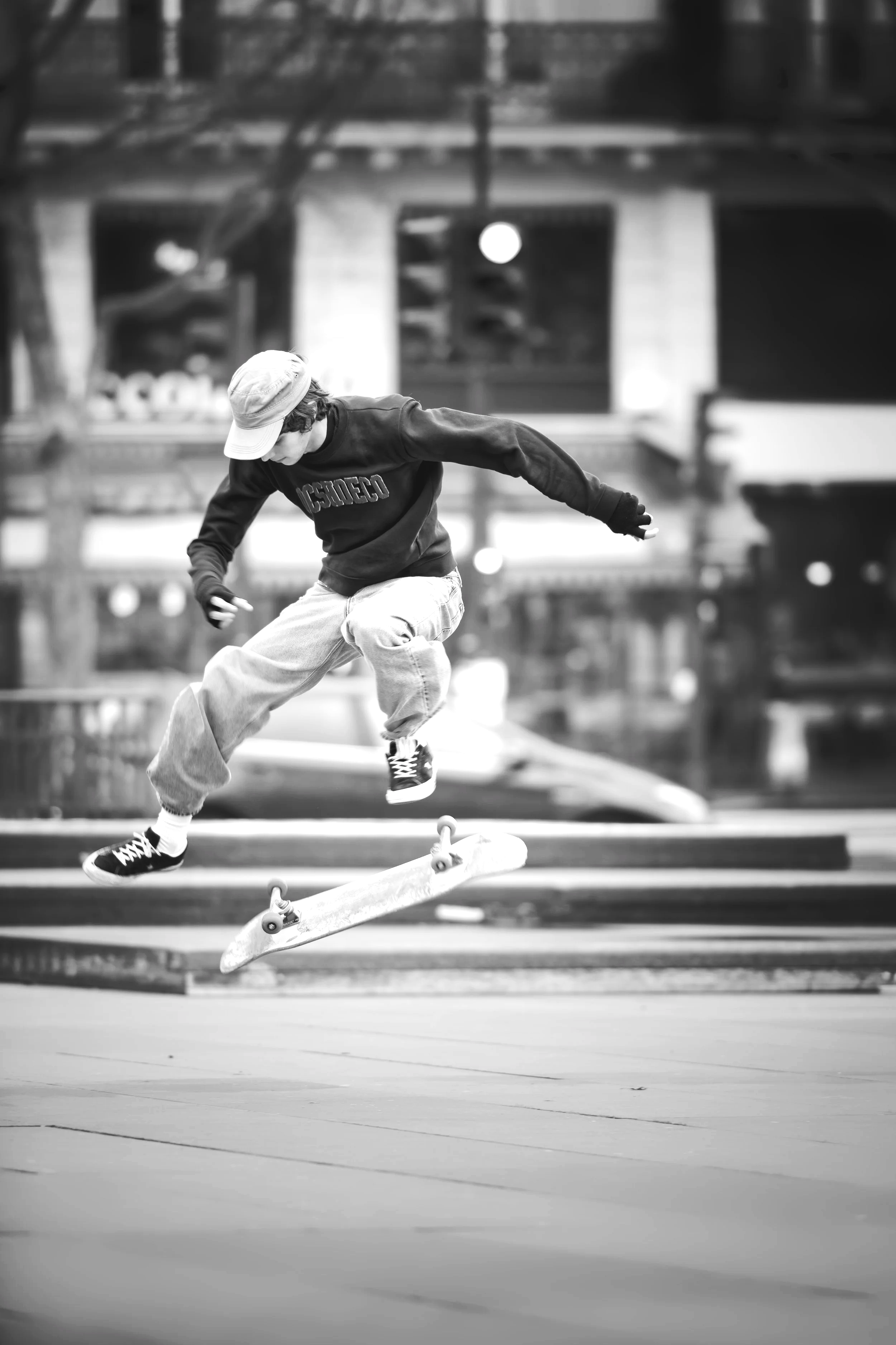 A young person skateboarding outdoors in an urban setting, captured mid-air in black and white.